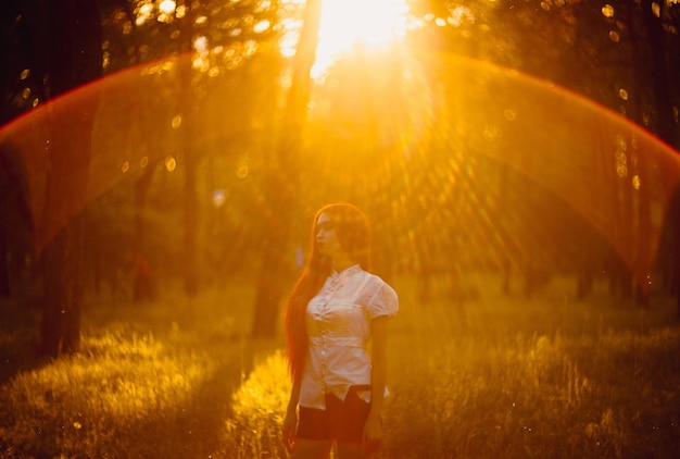 Piękna młoda kobieta z rudymi włosami w parku. Portret rudowłosej dziewczyny w parku o zachodzie słońca