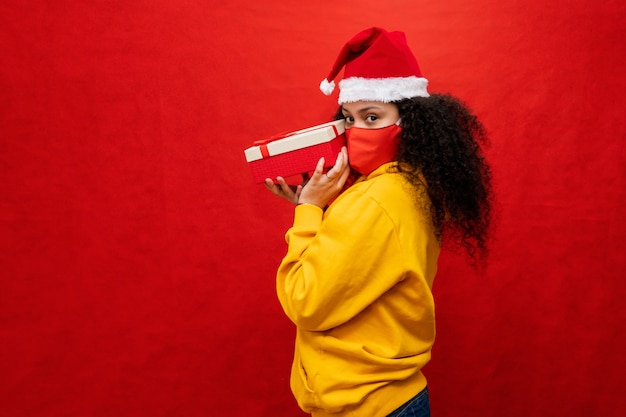 Piękna młoda kobieta z Santa hat i maską ochronną koronawirusa, trzyma pudełka na prezenty.