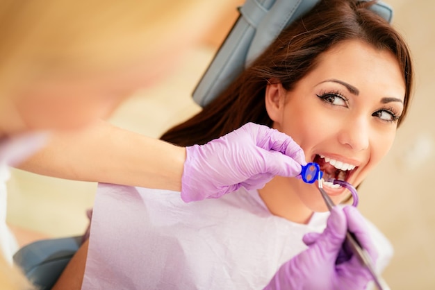 Piękna młoda kobieta z wizytą w gabinecie stomatologicznym. Siedzi na krześle, a dentysta naprawia jej zęby. Selektywne skupienie.