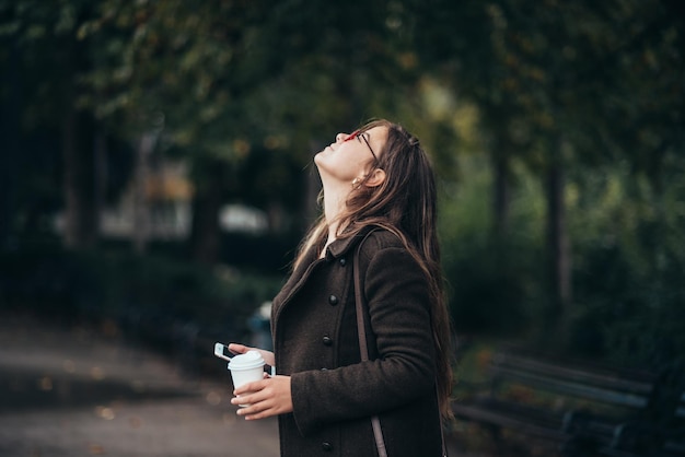 Piękna młoda kobieta za pomocą smartfona i pije kawę na wynos