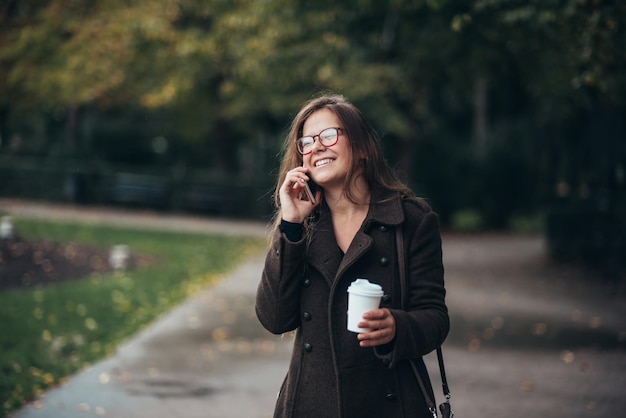 Zdjęcie piękna młoda kobieta za pomocą smartfona i pije kawę na wynos