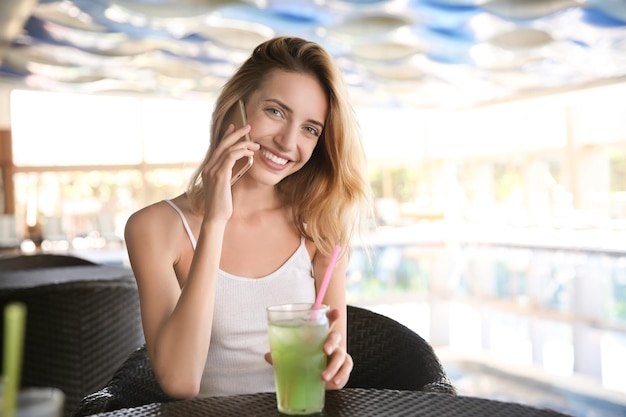 Piękna młoda kobieta ze szklanką lemoniady rozmawia przez telefon komórkowy w kawiarni