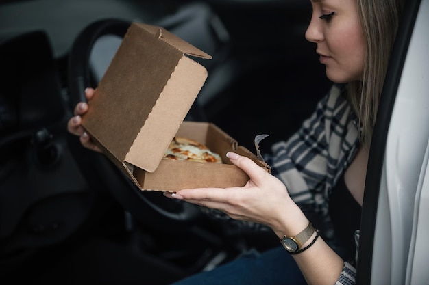 Zdjęcie piękna młoda kobieta zje lunch w swoim samochodzie z gotowaną pizzą