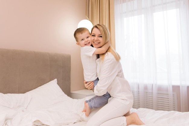 Piękna młoda mama bawi się i śmieje ze swoim dzieckiem uśmiechniętym synem w łóżku w sypialni szczęśliwa rodzina