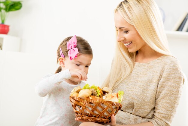 Piękna młoda mama daje swojej córce wiklinowy kosz ze świeżymi wypiekami, oferując jej różnorodne pyszne wypieki.