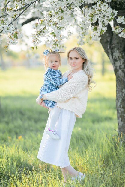 Piękna młoda mama z córeczką odpoczywa na pikniku w kwitnącym ogrodzie