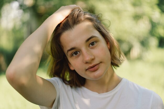 Zdjęcie piękna młoda nastolatka z modnymi włosami bob w białej koszulce w plenerze i patrząca na c...