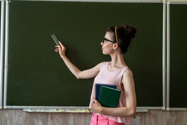 Piękna młoda nauczycielka lub studentka stojąca w pobliżu pustej tablicy