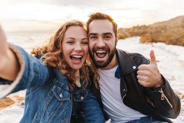 piękna młoda para kaukaska uśmiecha się i robi zdjęcie selfie podczas spaceru nad morzem