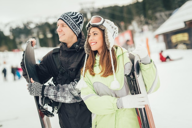 Piękna młoda para korzystających w ferie zimowe. Stoją z nartami i snowboardem i odwracają wzrok.