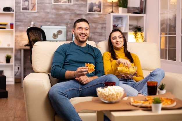 Piękna młoda para ogląda telewizję i je fast food na wynos w salonie