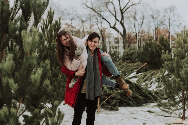 Piękna młoda para przyjechała wybrać drzewo. Zakochani Nowożeńcy wygłupiają się zimą. Ładna kobieta śmieje się na ramionach mężczyzny.