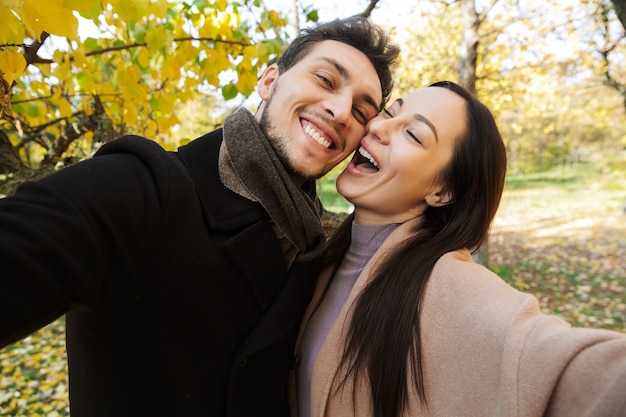 Piękna młoda para zakochana spędzająca razem czas w parku jesienią, robiąca selfie, przytulająca się