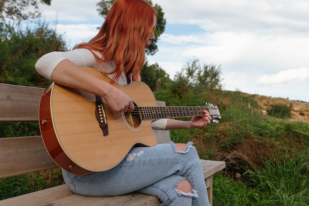 Zdjęcie piękna młoda redhaired dziewczyna gra na gitarze na zewnątrz