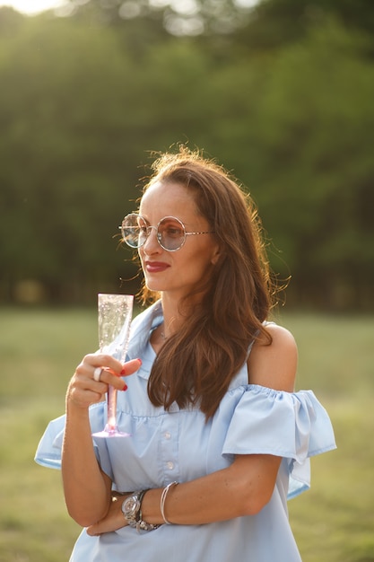 Piękna młoda smilling kobieta wewnątrz przy lampką szampana przy zielonym lato parkiem.