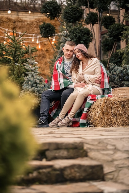 Piękna młoda szczęśliwa uśmiechnięta para owinięta szkockim kocem Zielone choinki na tle Zimowe ferie Czekam na nowy rok