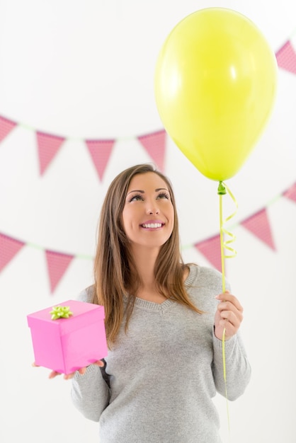 Piękna młoda uśmiechnięta kobieta gospodarstwa różowy prezent urodzinowy i balon.