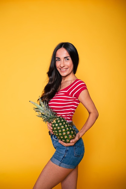 Piękna młoda uśmiechnięta kobieta z ananasem w dłoniach na pomarańczowym tle Owoce tropikalne Zdrowe odżywianie