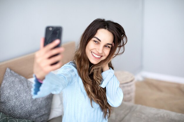 Piękna młoda uśmiechnięta kobieta z telefonem w dłoniach bierze selfie. Styl życia.