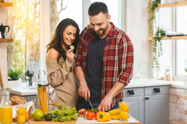 Piękna młoda uśmiechnięta szczęśliwa para jest opowiadająca i uśmiechnięta podczas gdy gotujący zdrowego jedzenie w kuchni w domu.