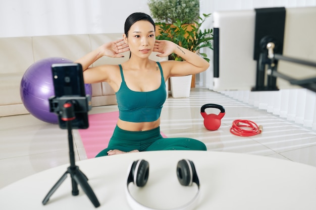 Zdjęcie piękna młoda wietnamka ćwicząca w salonie i nagrywająca się na zajęcia online