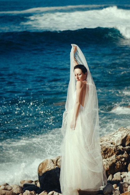 Piękna modelka w białej sukience pozuje nad morzem
