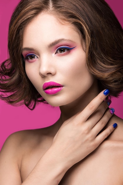 Piękna modelka z jasnym makijażem i kolorowym lakierem do paznokci Piękna twarz Krótkie kolorowe paznokcie Zdjęcie zrobione w studio na różowym tle