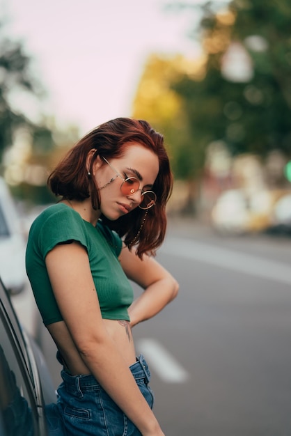 Piękna modna młoda kobieta w okularach pozowanie w pobliżu samochodu