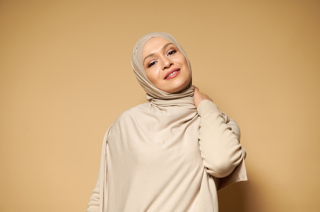Piękna muzułmańska kobieta w hidżabie słodkie uśmiechy, stwarzając na beżowej powierzchni z miejsca na kopię