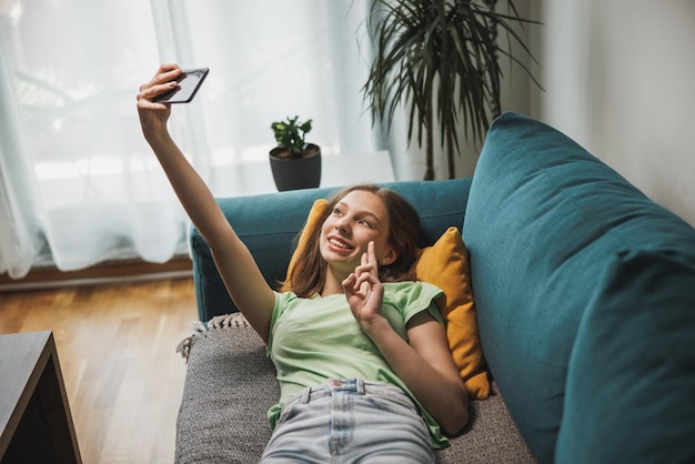 Piękna nastolatka dziewczyna co selfie z inteligentnego telefonu, mając jednocześnie wolny czas w swoim domu.