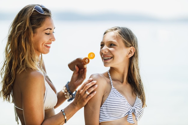 Piękna nastolatka i jej młoda matka używają kremu z filtrem przeciwsłonecznym, ciesząc się czasem na plaży.