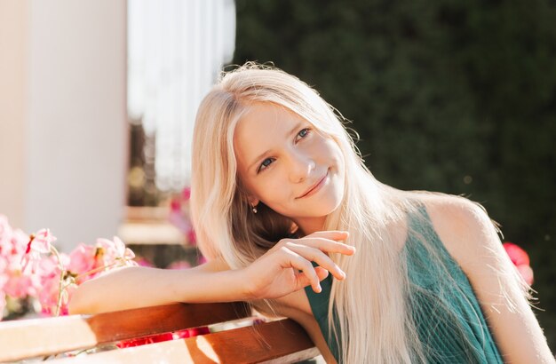 Piękna nastolatka z długimi blond włosami siedzi na ławce w kwitnącym parku