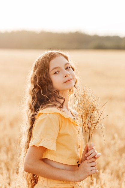Piękna nastolatka z długimi włosami chodzenie po polu pszenicy w słoneczny dzień. Portret na zewnątrz. Uczennica relaksująca