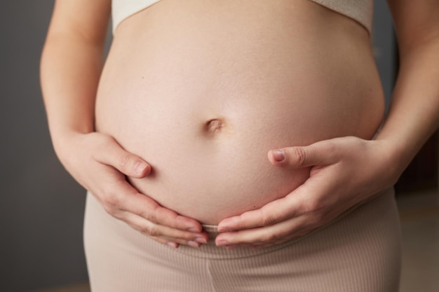 Piękna, nieznana, w ciąży kobieta z gołym brzuchem stoi w domu, w wnętrzu, przyszła matka dotyka swojego brzucha, wyrażając miłość do swojego przyszłego dziecka.