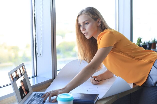 Piękna nowoczesna kobieta zapisuje coś na planie i używa laptopa