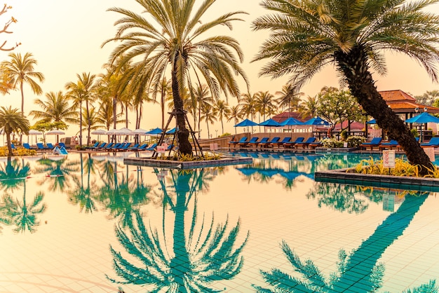 piękna palma z parasolem w basenie w luksusowym hotelu o wschodzie słońca. koncepcja wakacji i wakacji