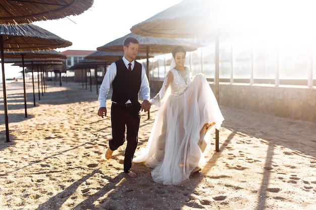 Piękna panna młoda i pan młody spacerują wzdłuż piaszczystej plaży trzymając się za ręce Szczęśliwej pary ślubnej na plaży morskiej