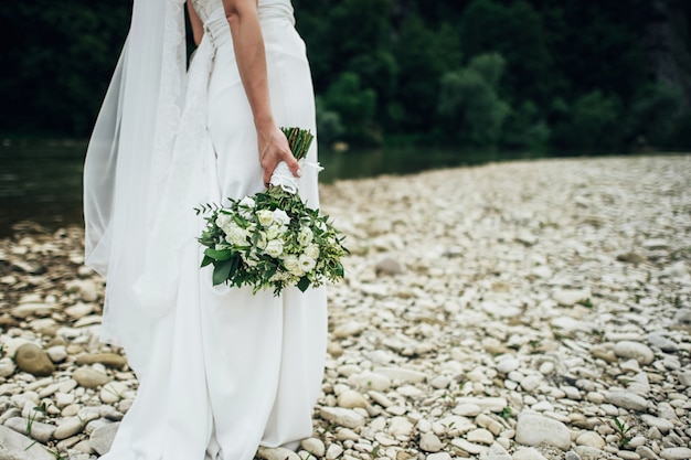 Piękna panna młoda w ślubnej sukni trzyma dużego ślubnego bukiet. Zbliżenie panny młodej nogi w sukni ślubnej w białe trampki. Bukiet ślubny w rękach