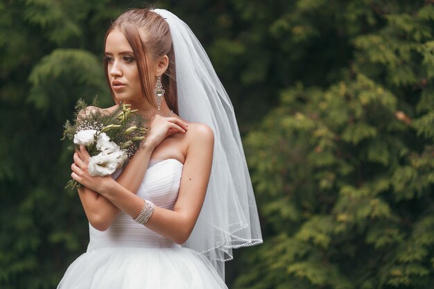 Piękna Panna Młoda W Wspaniałej Sukni ślubnej Pozującej Wśród Zieleni Na Ulicy. Koncepcja Panny Młodej Dla Sukienek Reklamowych