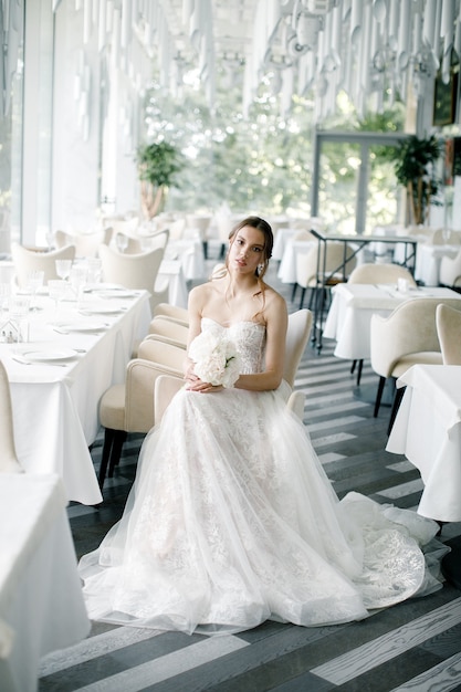 Piękna panna młoda z bukietem w ręku siedzi w dniu ślubu restauracji