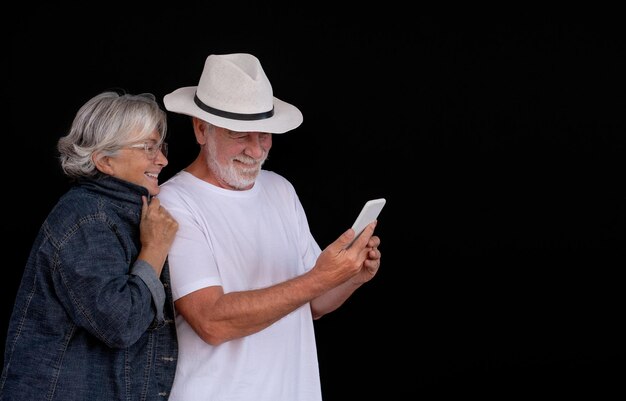 Piękna para seniorów uśmiecha się przy użyciu nowoczesnej technologii patrząc na ten sam smartfon Dwóch beztroskich i szczęśliwych ludzi na emeryturze