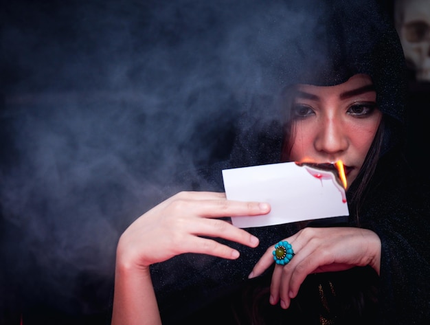 Piękna poważna tajemnicza kobieta w ciemności trzymająca płonące karty tarota, aby wróżka czytała przyszłość