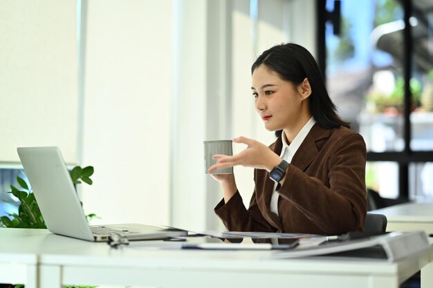 Piękna pracownica firmy lub menedżerka z filiżanką kawy i laptopem na biurku
