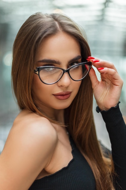 Piękna profesjonalna menedżerka biznesowa w czarnym eleganckim topie zakłada modne okulary w szklanym biurowcu