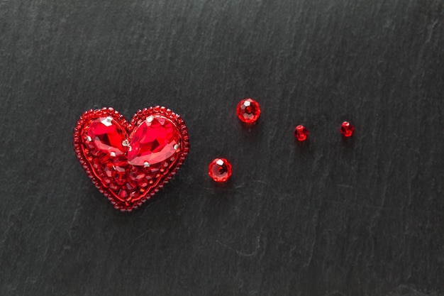 Piękna ręcznie haftowana broszka z czerwonym sercem z kryształkami z góry płaski widok na ciemne tło