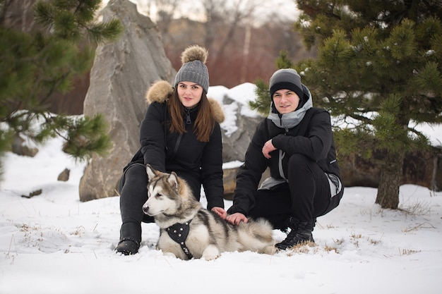 Piękna rodzina, mężczyzna i dziewczyna w zimowym lesie z psem. Baw się z psem husky syberyjskim.