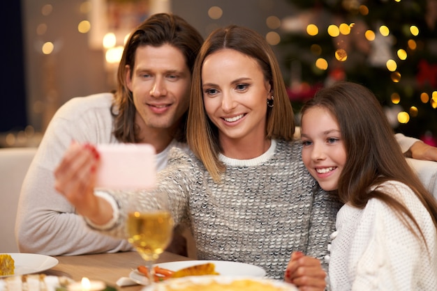 Piękna rodzina świętująca Boże Narodzenie w domu i robiąca selfie