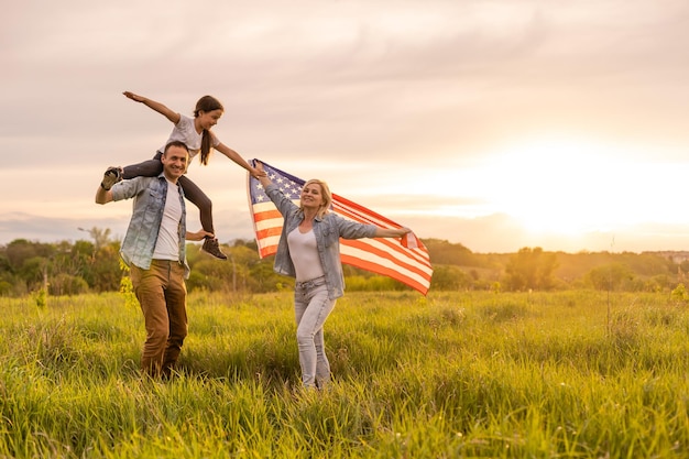 Piękna rodzina z amerykańską flagą w polu o zachodzie słońca. Święto Niepodległości, 4 lipca.