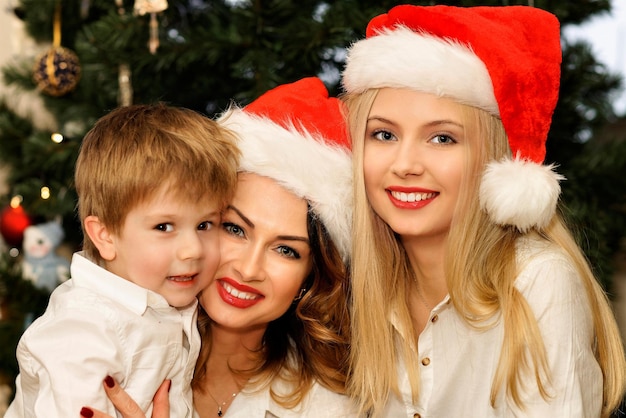 Piękna rodzina z matką i córką w czerwonych czapkach Mikołaja i synem na choince. Choinka na tle.
