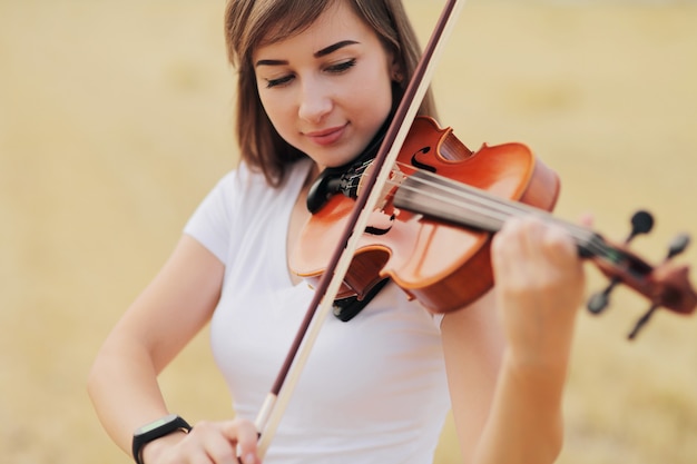 Piękna romantyczna dziewczyna z luźnymi włosami, grając na skrzypcach w polu.